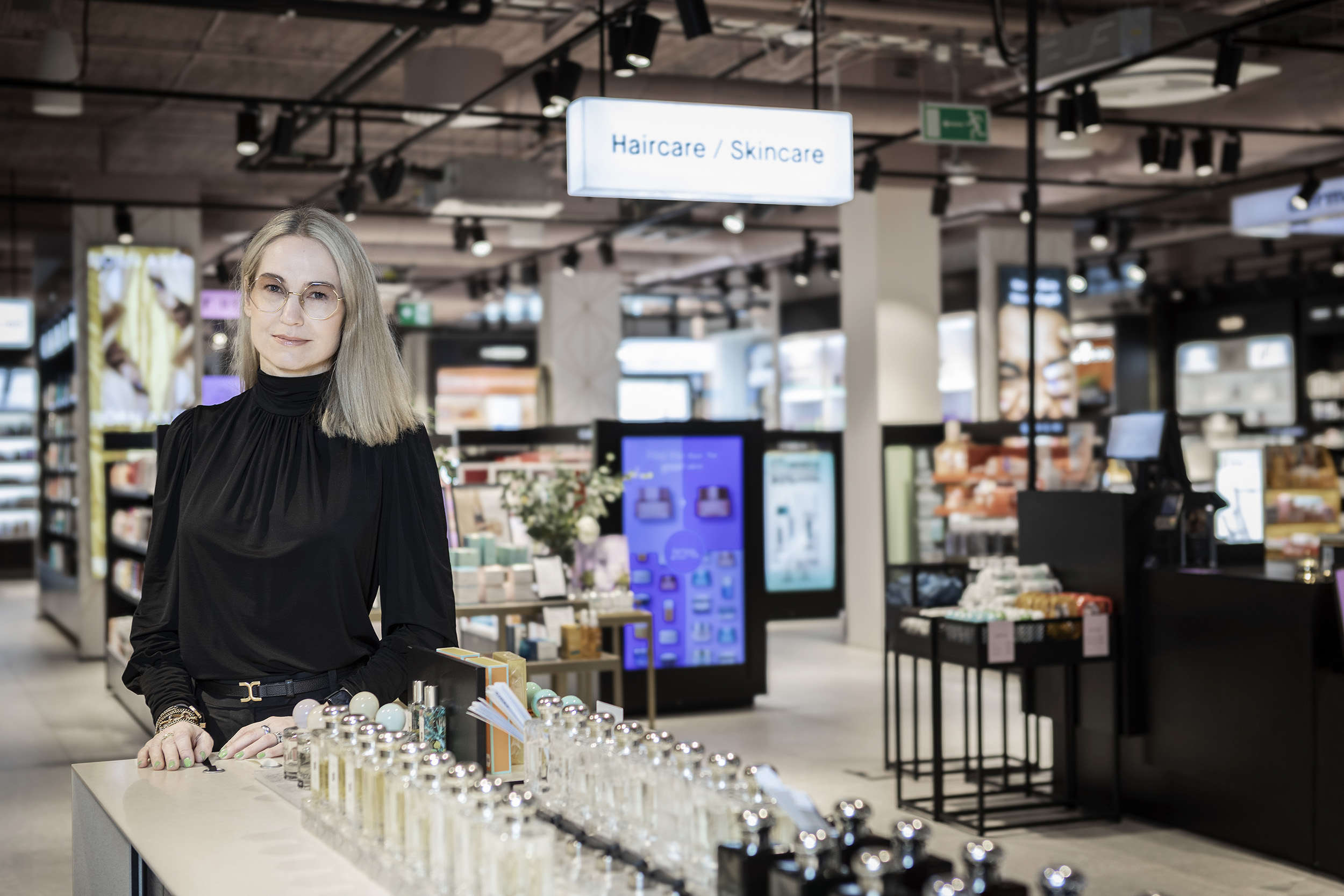 Carola Lundel, vd för Kicks, står i en butik. Framför henne står ett bord med skönhetsprodukter.